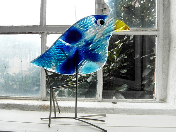 Glasvogel in Blautönen auf Edelstahlfüßen vor Fenster